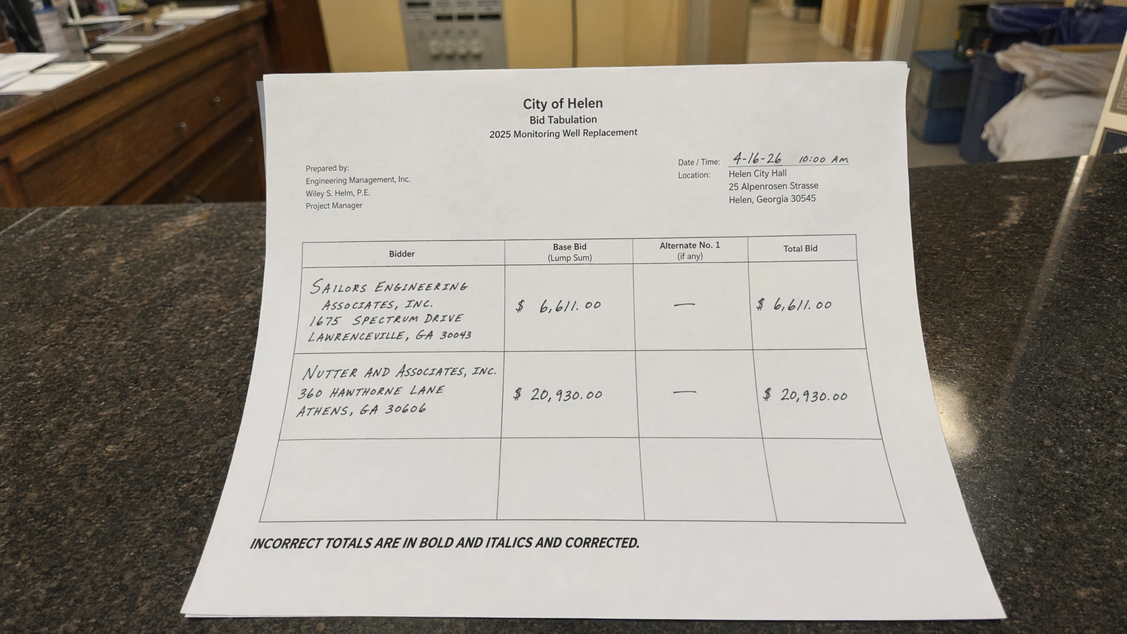 The bid tabulation for the 2025 Monitoring Well Replacement, prepared by Engineering Management, Inc. Project Manager Wiley S. Helm, P.E., photographed at the City Clerk's counter at Helen City Hall on Tuesday morning. The tabulation's disclaimer — 'INCORRECT TOTALS ARE IN BOLD AND ITALICS AND CORRECTED' — is visible at the bottom left. (Photo: Bavarian Brainrot / Margaret Holcomb)